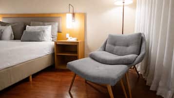 A hotel room with a bed, a chair, a bedside table, and a lamp.