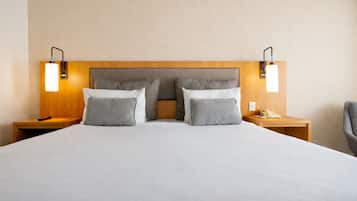 Uma cama grande com cabeceira de madeira, duas mesas de cabeceira com abajures e uma cadeira.