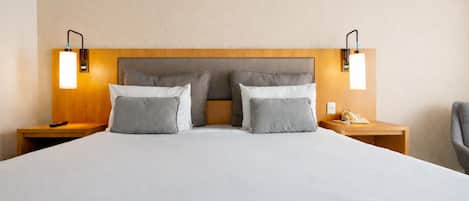 Una cama grande con cabecera de madera, dos mesitas de noche con lámparas y una silla.