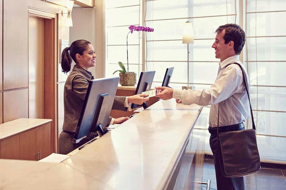A hotel reception desk with a receptionist and a guest exchanging documents.
