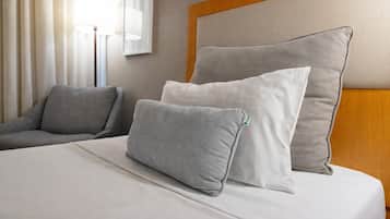 A neatly made bed with two pillows, a grey sofa, and a lamp in a hotel room.