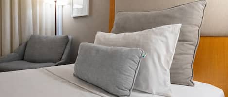 Una cama bien hecha con dos almohadas, un sofá gris y una lámpara en una habitación de hotel.