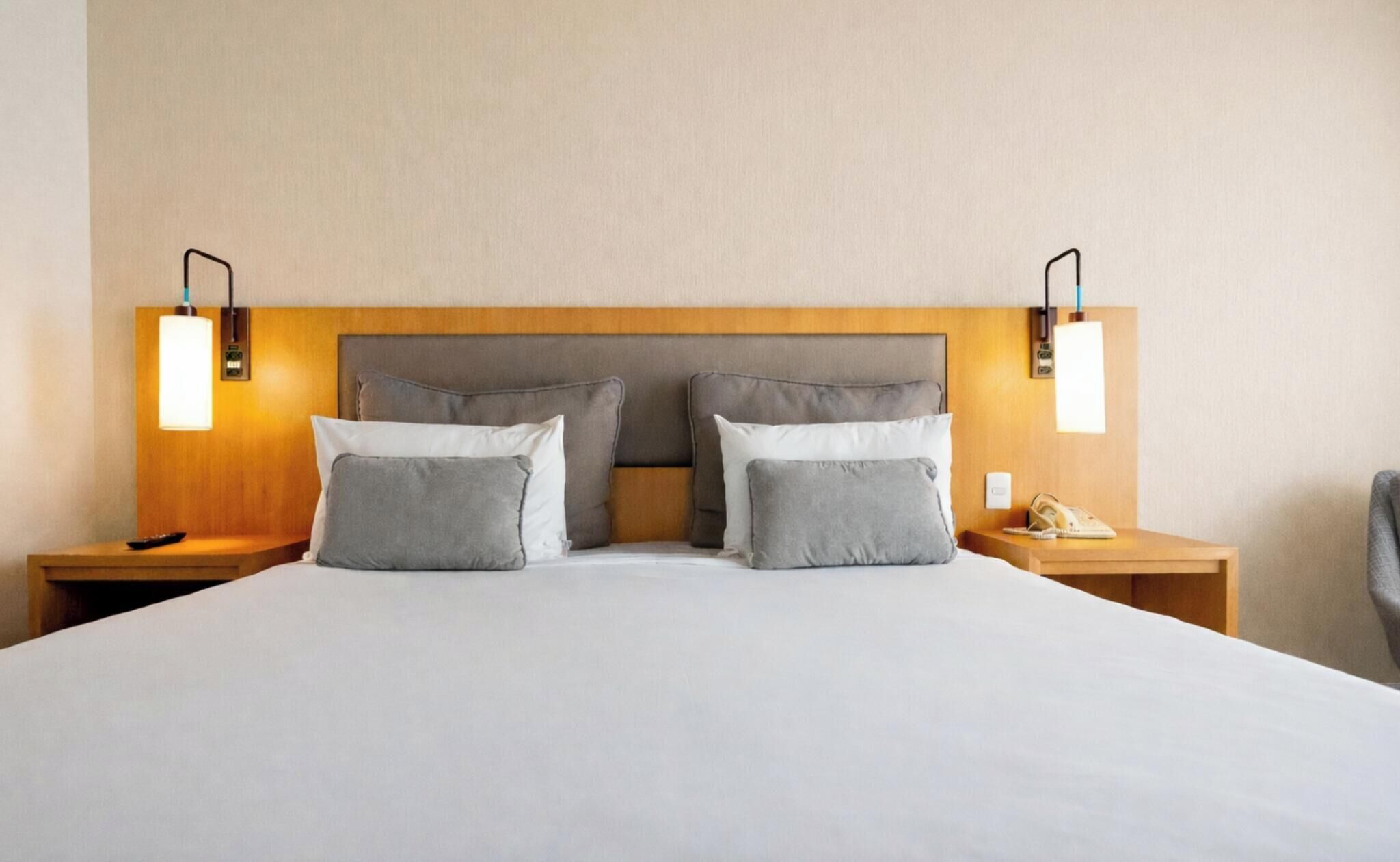Ein Hotelzimmer mit einem großen Bett, zwei Nachttischen, einem Holz-Kopfteil und Wandleuchten.