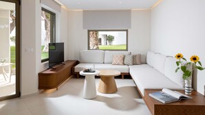 A modern living room with a sofa, a coffee table, a TV, and a window with a view of the outdoors.