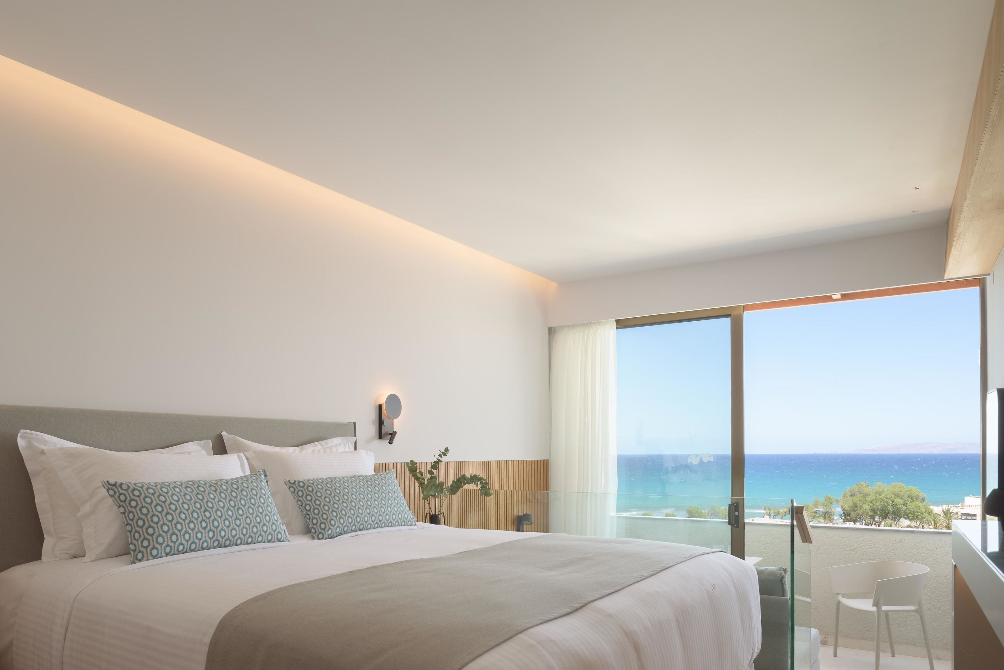 Una habitación de hotel moderna con una cama grande, una mesita de noche, un espejo y vista al mar.