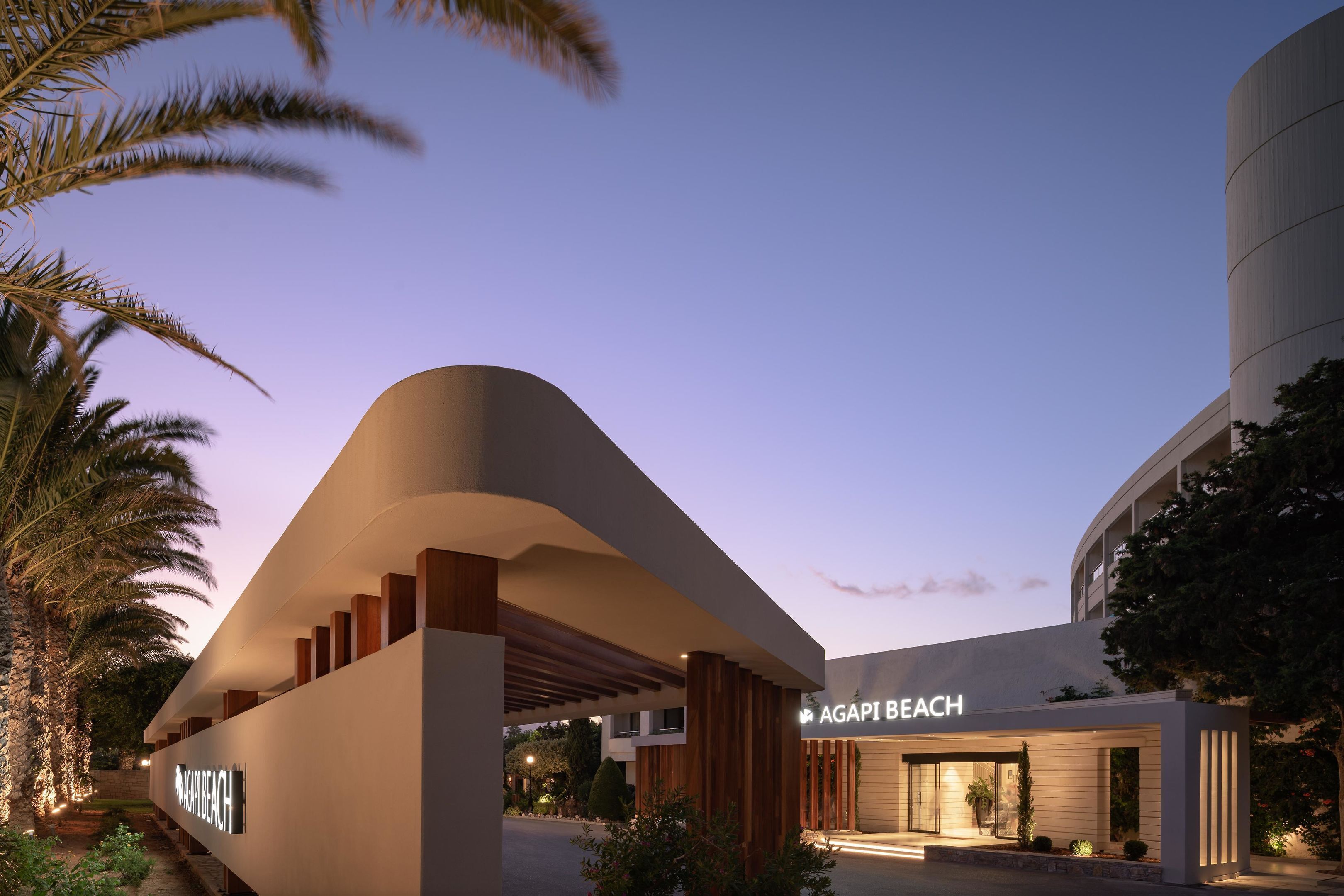 A modern building with a curved facade and a sign reading "AGAPI BEACH".