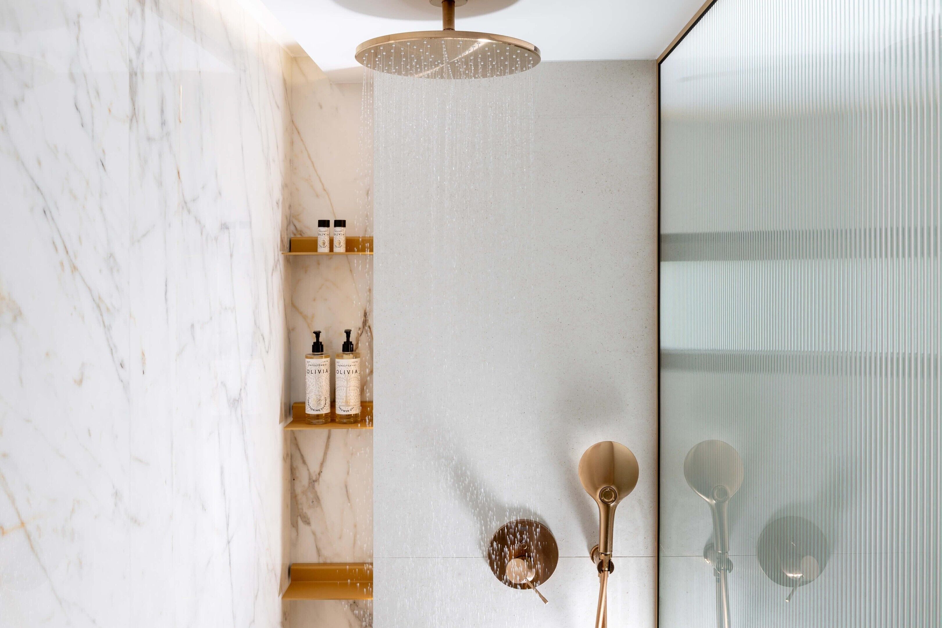 A modern bathroom with a marble wall, a shower with a gold showerhead, and a glass shower enclosure.