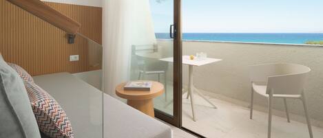 Un balcon avec une porte vitrée, une petite table ronde sur laquelle repose un livre, deux chaises blanches et une vue sur la mer.