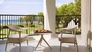 A balcony with two chairs, a table with breakfast, and a view of the sea and greenery.