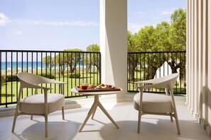 A balcony with two chairs, a table with breakfast, and a view of the sea and greenery.