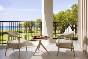 Un balcón con dos sillas, una mesa con desayuno y vistas al mar y al follaje.