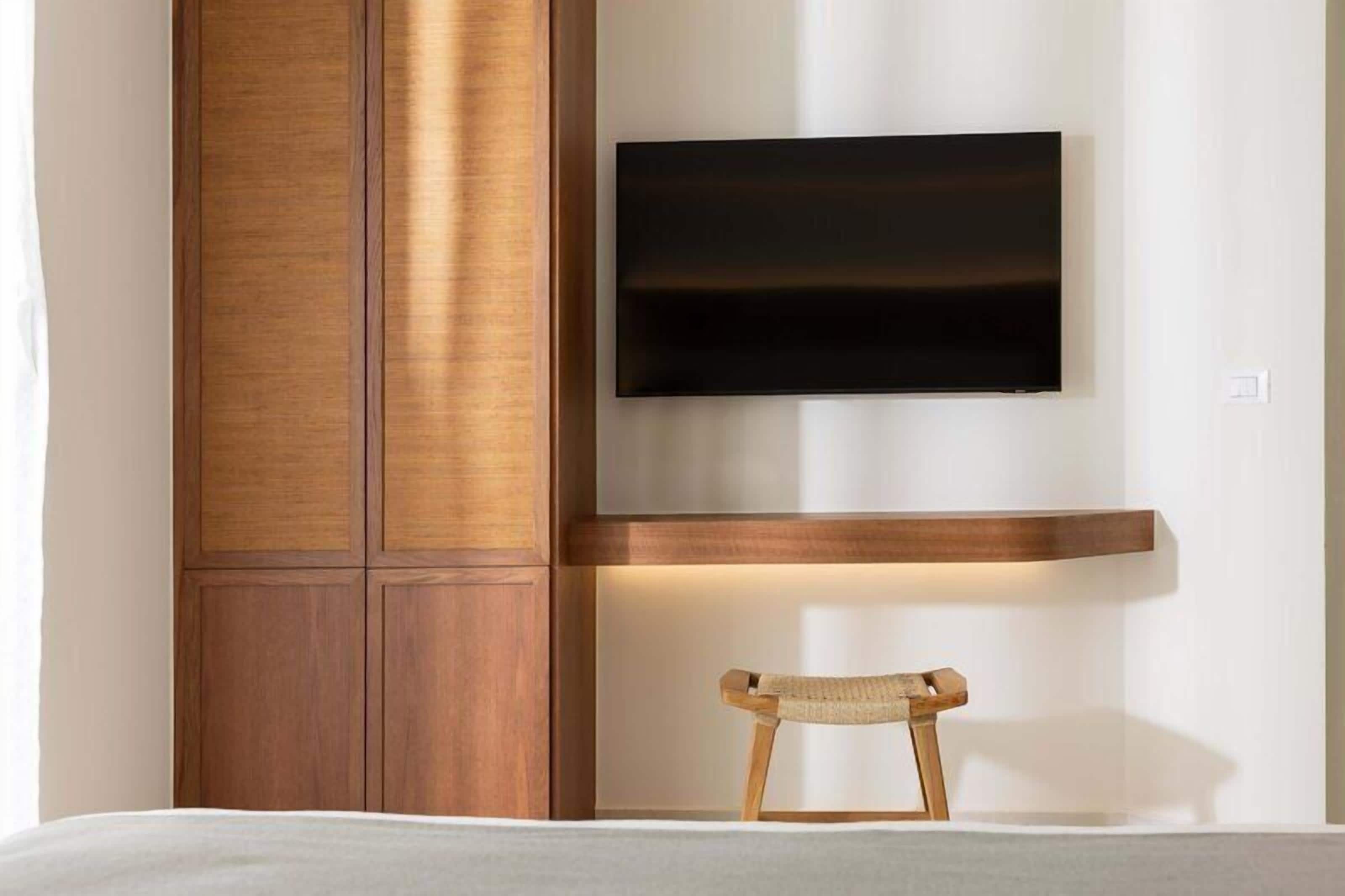 A modern room with a wooden cabinet, a mounted flat-screen TV, and a small wooden stool.