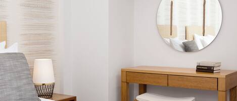 A neatly arranged bedroom with a bed, bedside table, lamp, and a wooden desk with a chair.