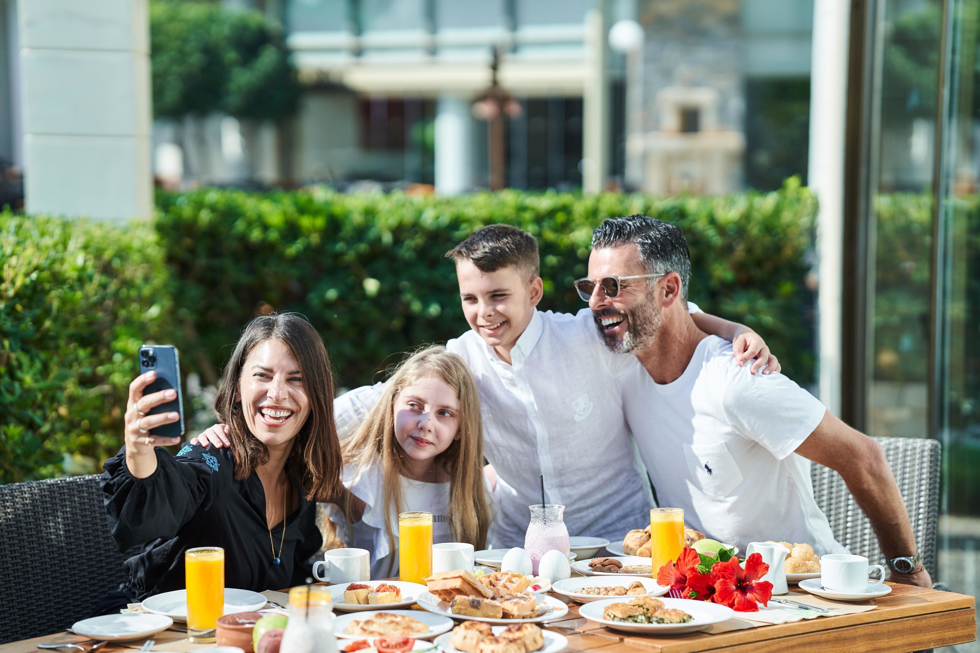 A group of people seated at an outdoor table with breakfast items, including eggs, pastries, and drinks.