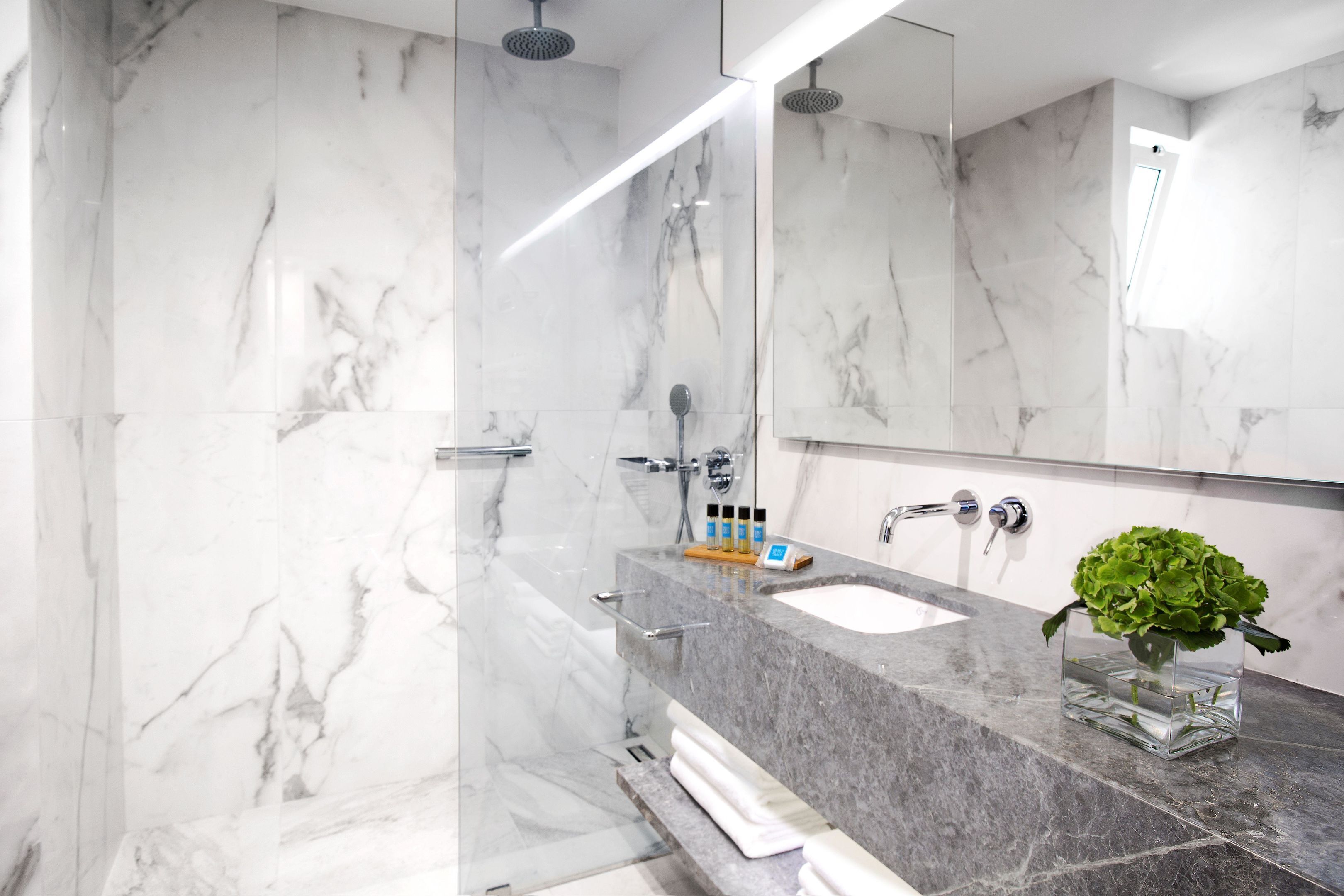 A modern bathroom with marble walls, a glass shower enclosure, a sink with a marble countertop, and a mirror.