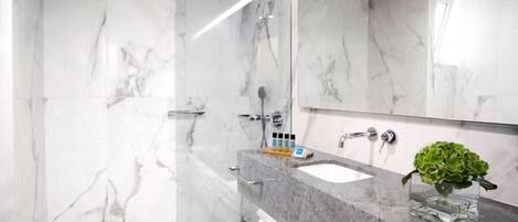 A modern bathroom with marble walls, a glass shower enclosure, a sink with a marble countertop, and a mirror.