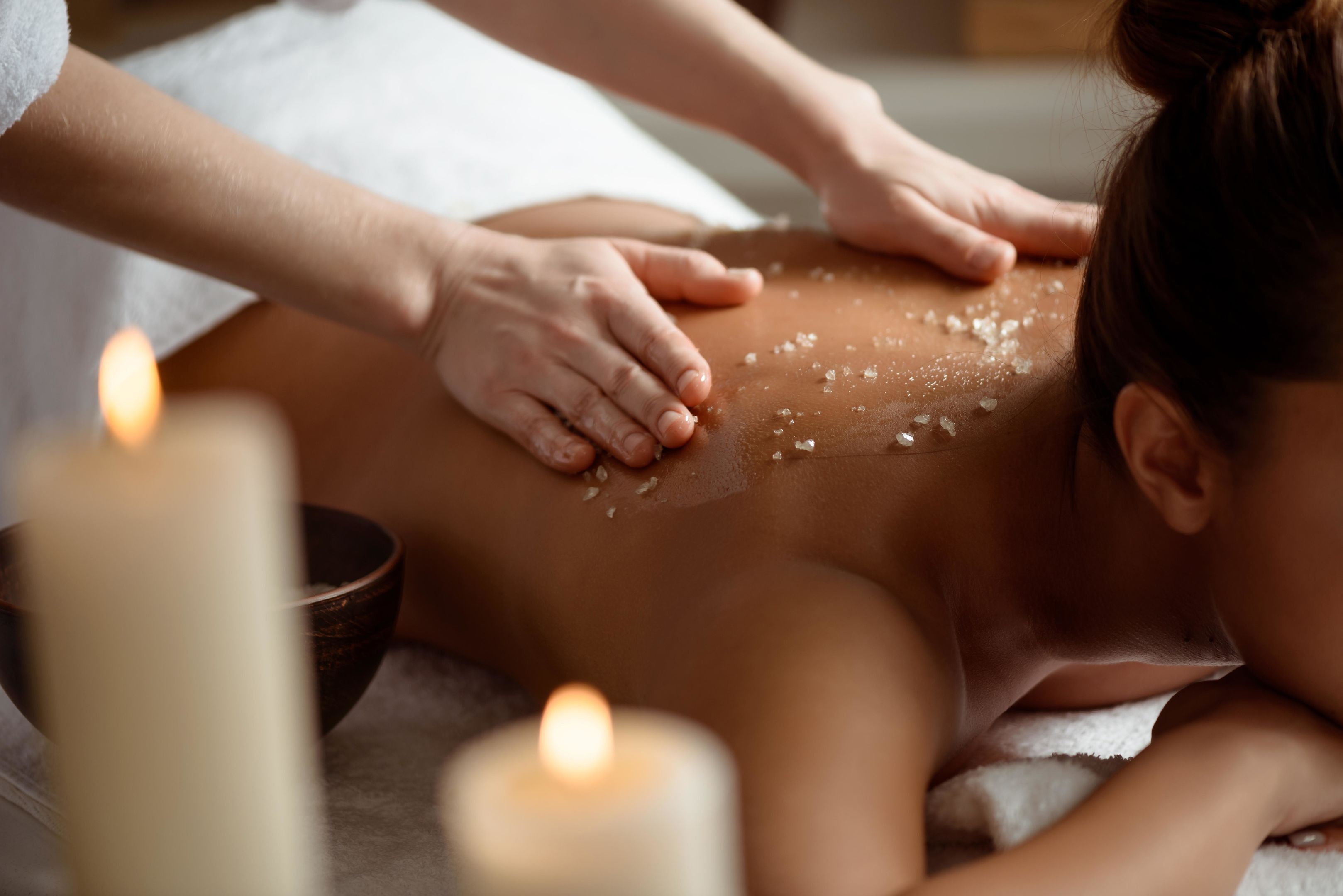 Une personne reçoit un massage du dos, du sel étant appliqué sur sa peau.