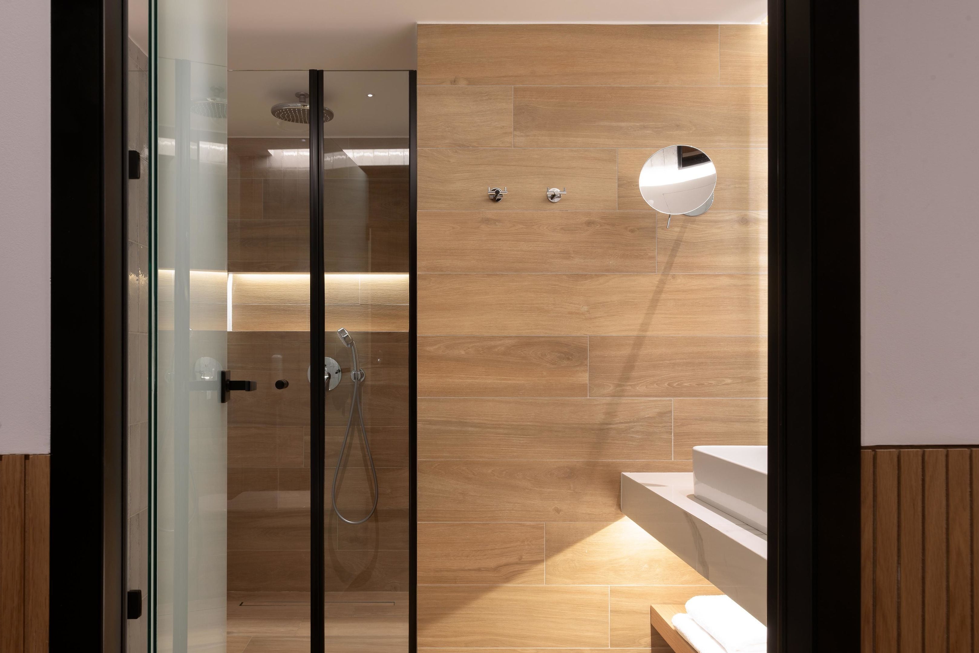 A modern bathroom with a glass shower enclosure, wooden wall tiles, and a white sink.