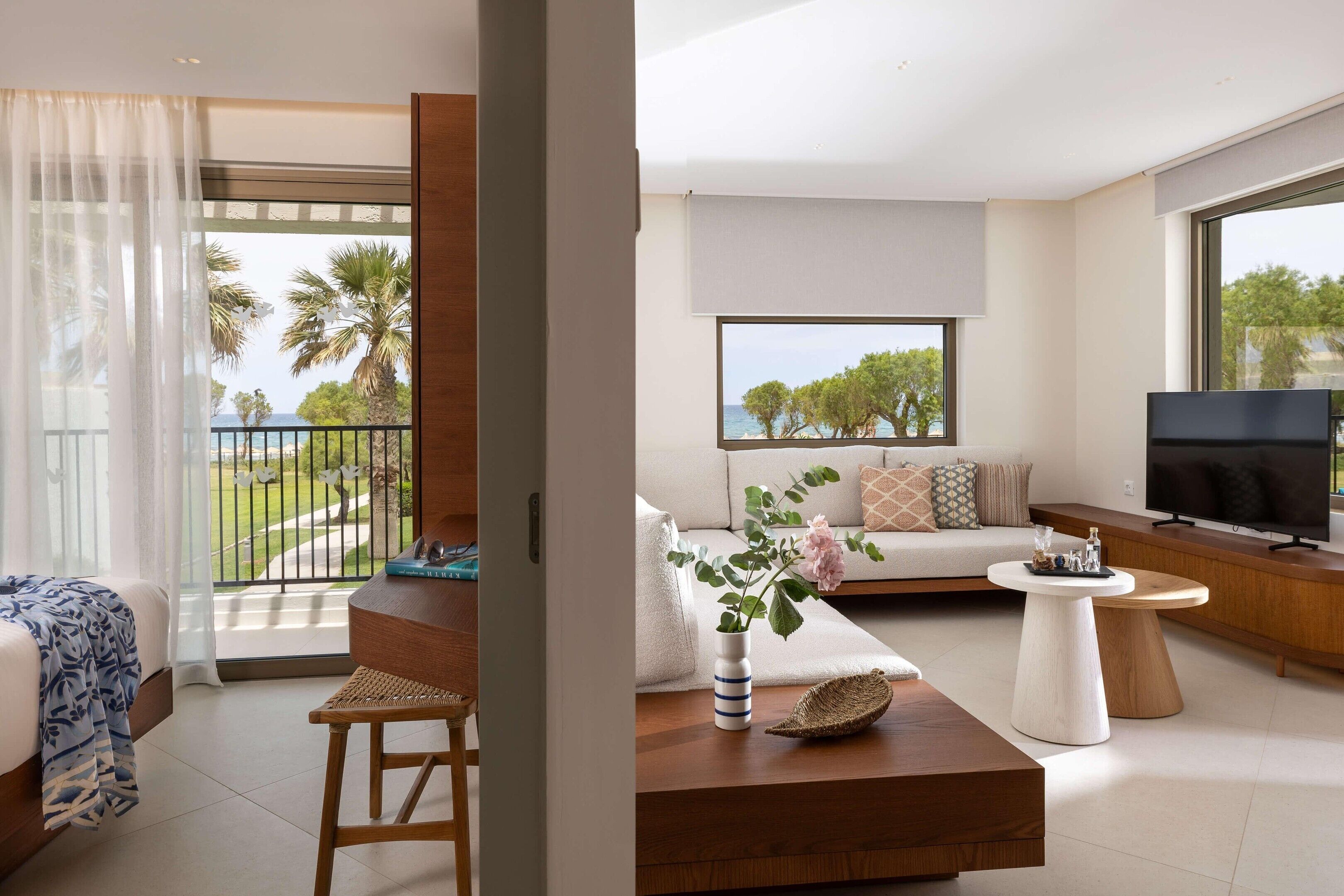 Una sala de estar moderna con un sofá, un televisor y un balcón con vista a palmeras.