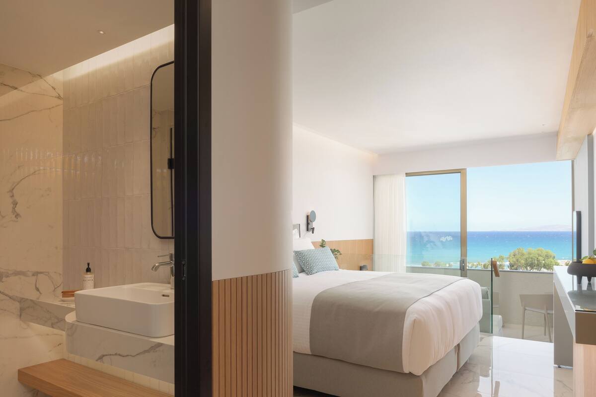 A modern bedroom with a large bed, a bathroom with a marble sink, and a view of the sea.