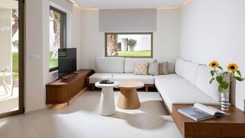 A modern living room with a sofa, a coffee table, a TV, and a window with a view of greenery.