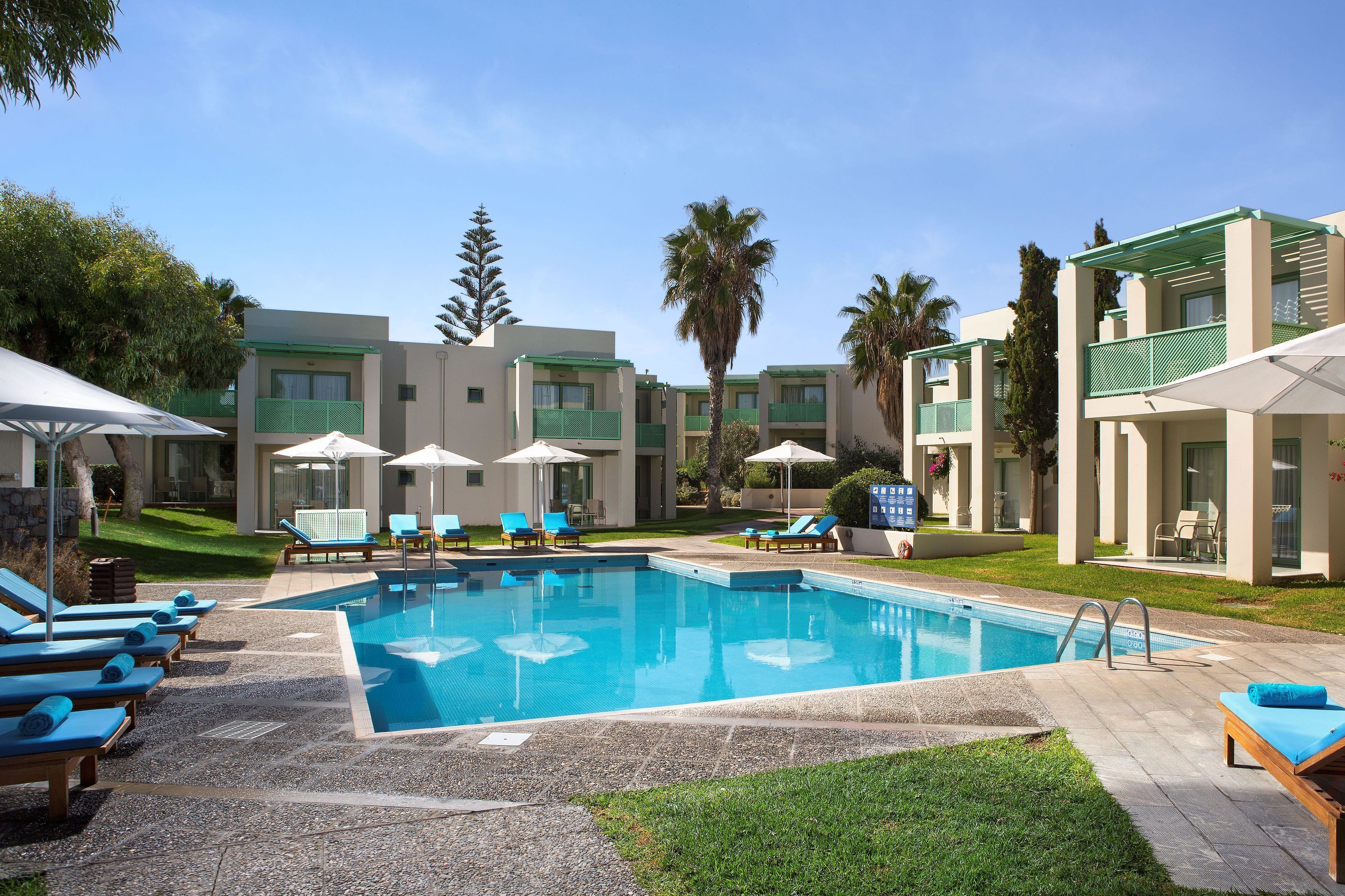 Uma área de piscina com espreguiçadeiras, guarda-sóis e um céu azul límpido.