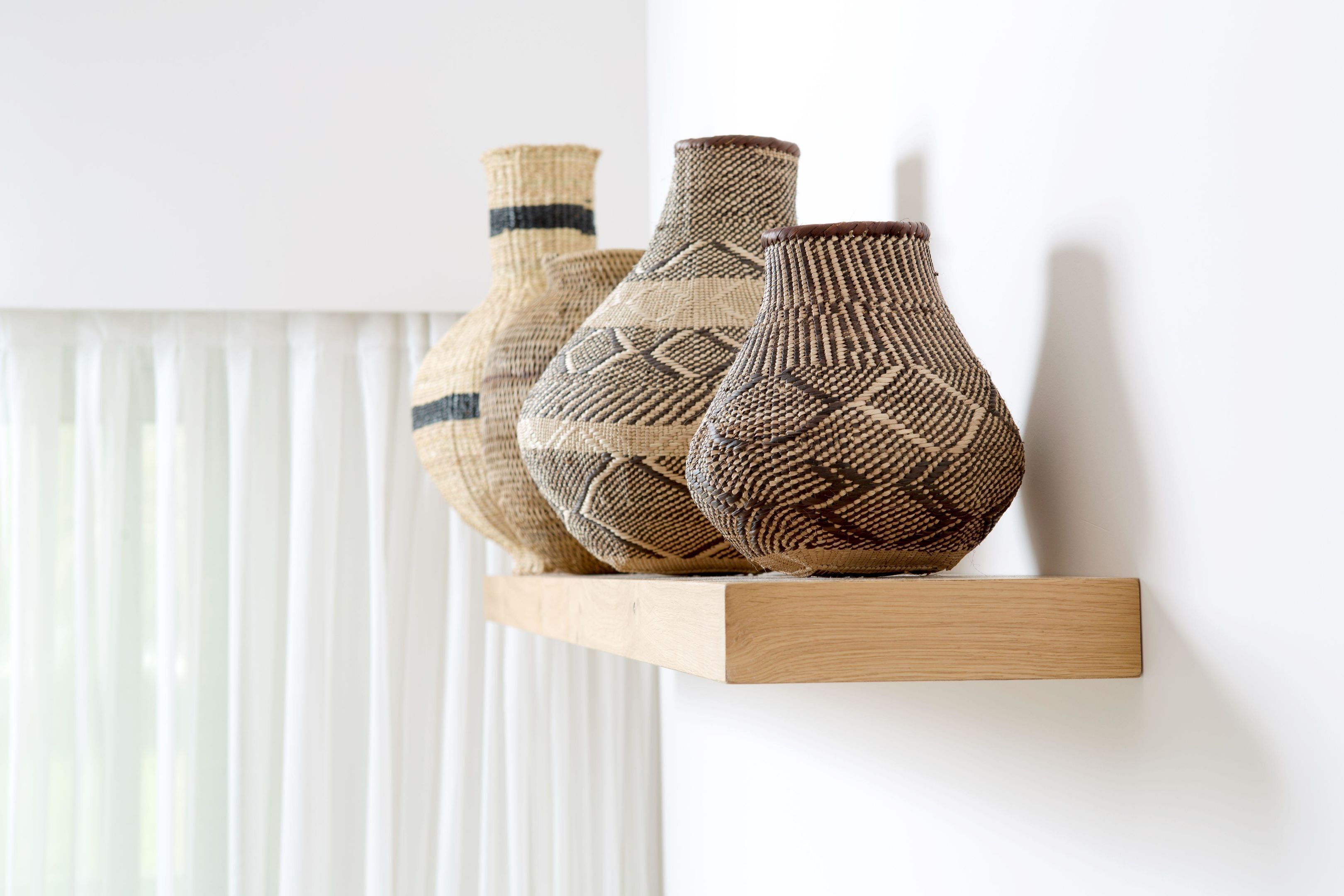 Three woven vases on a wooden shelf against a white wall.