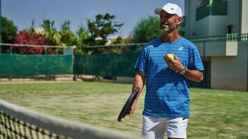A tennis court with a net, a person holding a tennis ball and racket, and a building in the background.