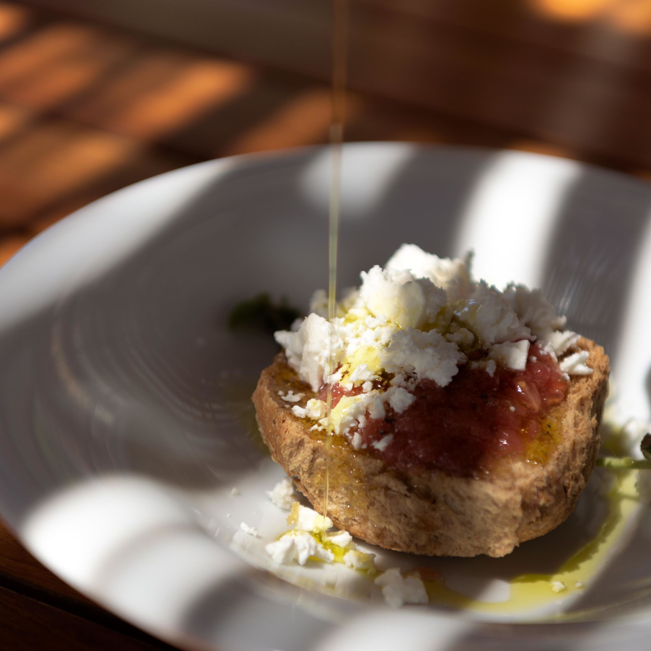 A white plate with a food item topped with cheese and sauce, and a drizzle of olive oil.