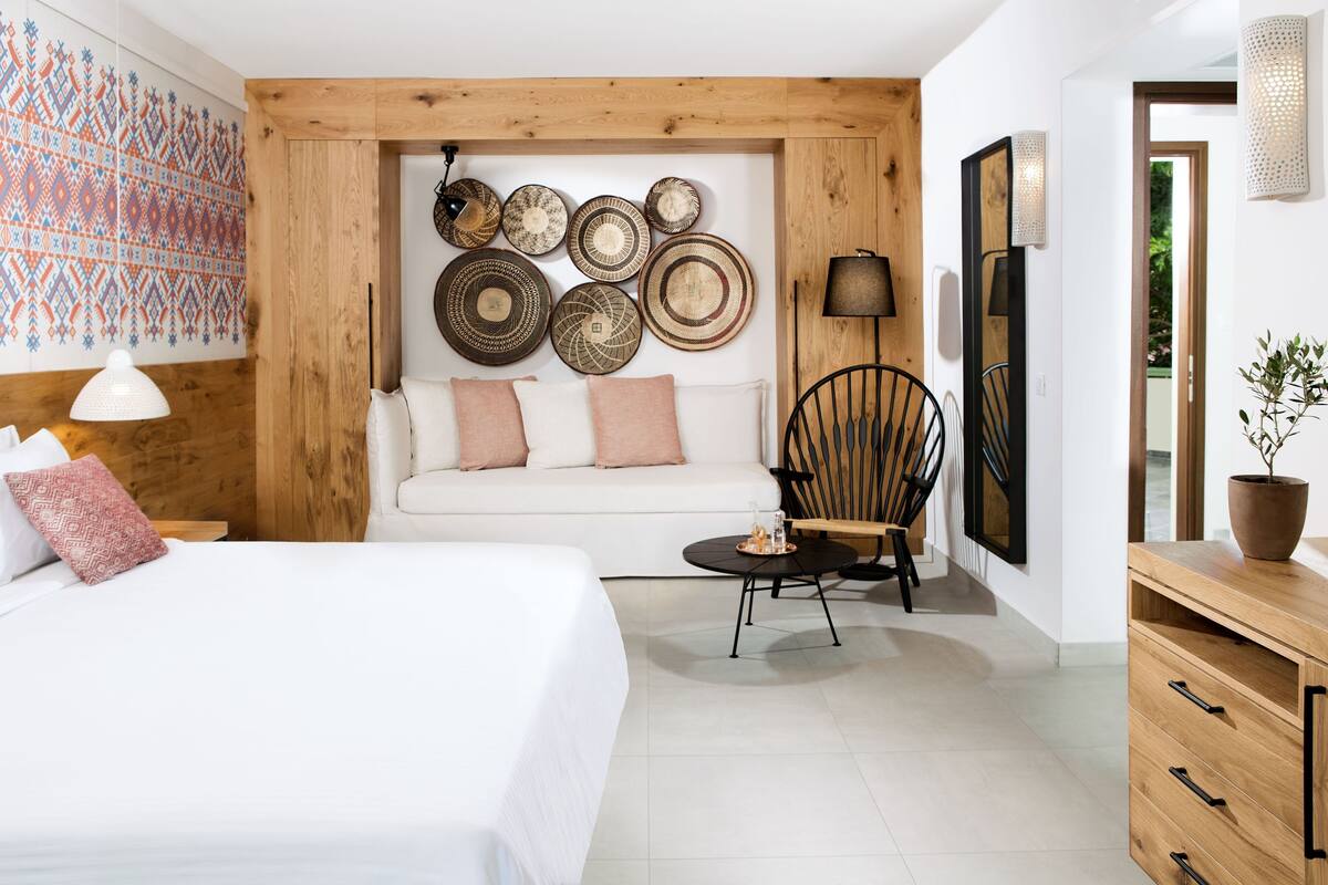 A modern room with a bed, a sofa, a dining table, and a chair. There are decorative plates on the wall and a potted plant on the side.