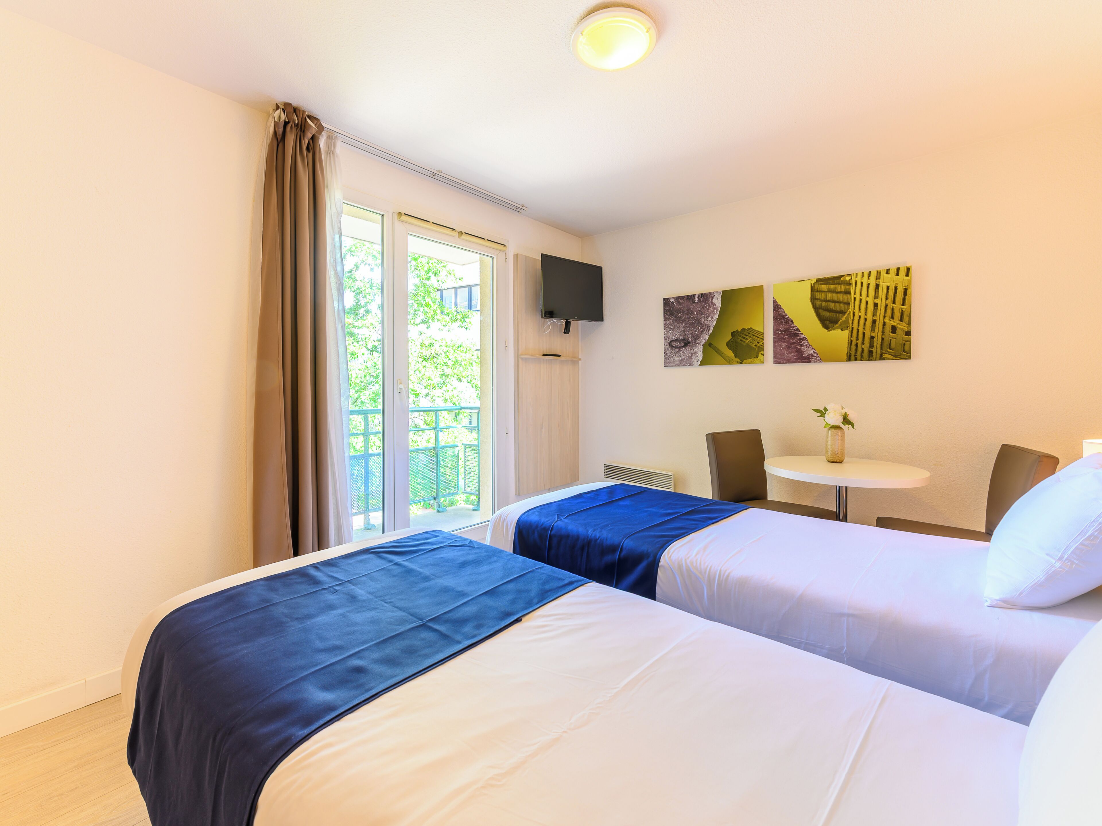 Habitación de hotel con dos camas, una mesita pequeña, una silla y un televisor en la pared.