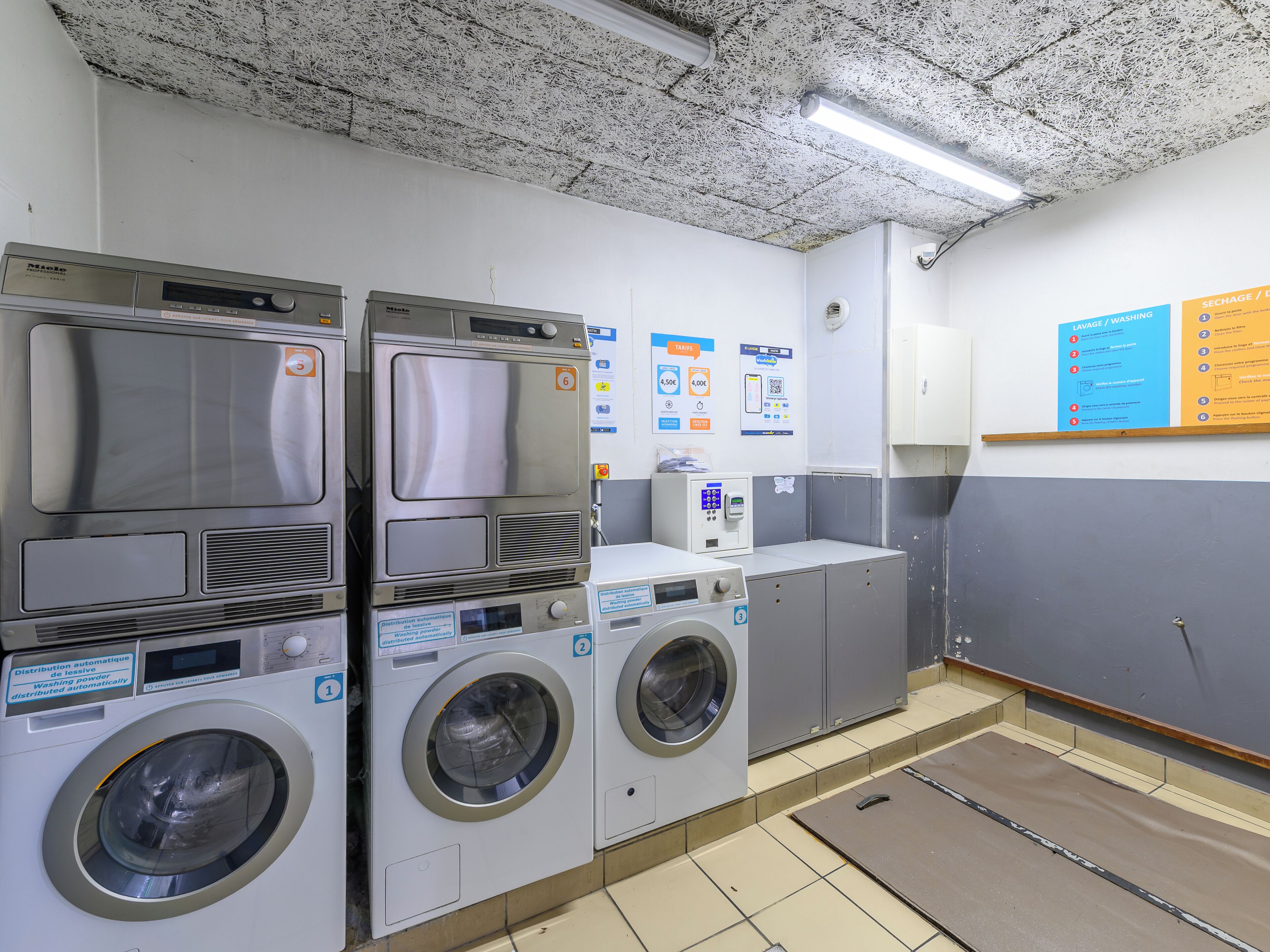 A laundry facility with multiple washing machines and dryers, a water dispenser, and instructional posters on the wall.