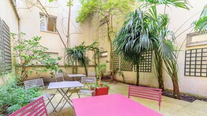 Un patio con una mesa y sillas rosadas, rodeado de plantas y árboles.