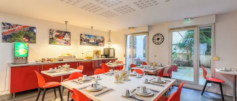 Un coin repas avec des chaises rouges, une table blanche et un espace cuisine comprenant un réfrigérateur et un évier.