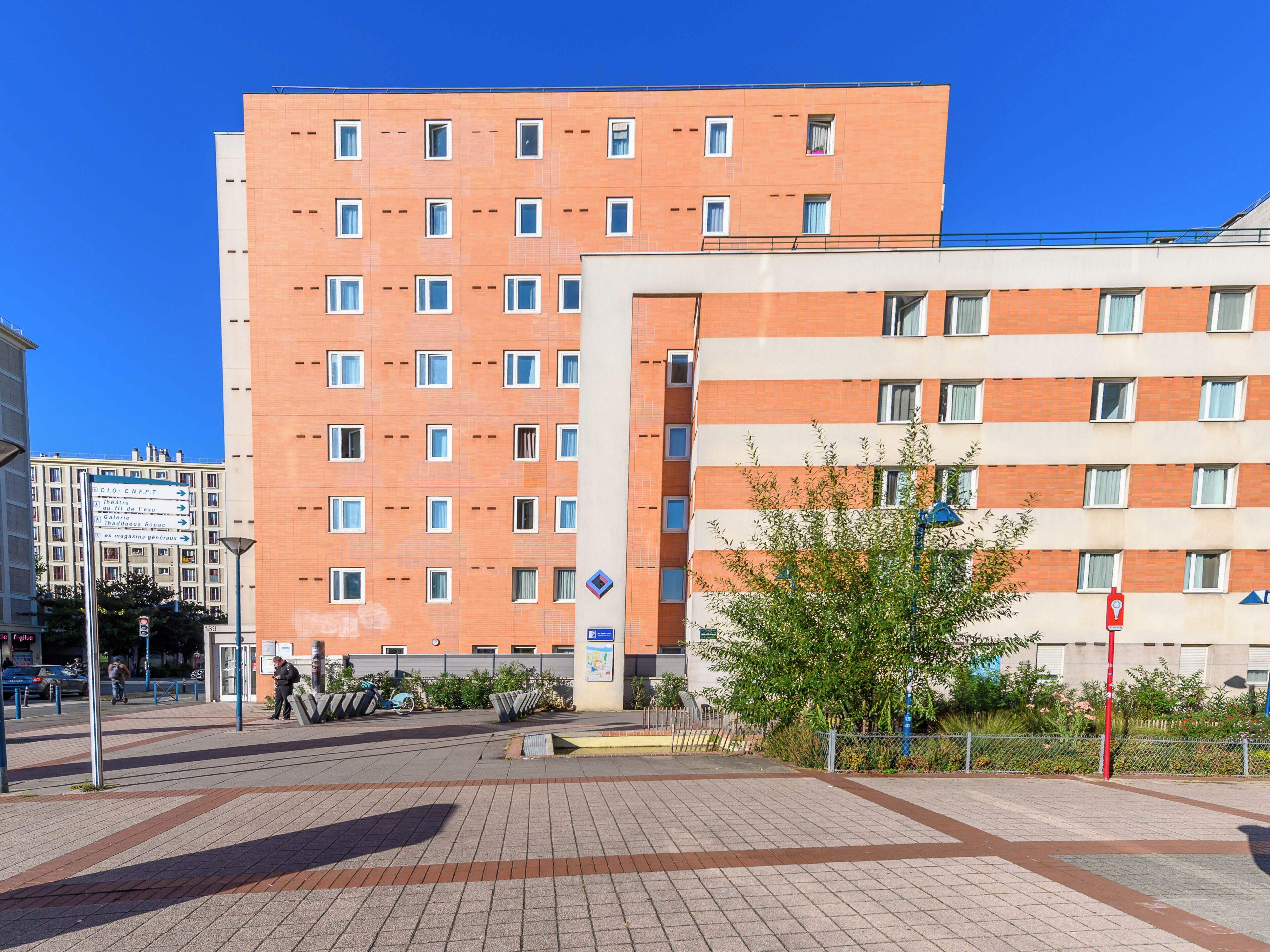 A multi-story building with a uniform facade, a pedestrian area with a paved walkway, and a clear blue sky.