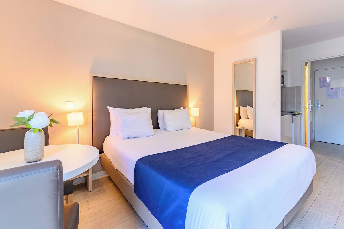 A hotel room with a bed, bedside tables, a desk, and a mirror.
