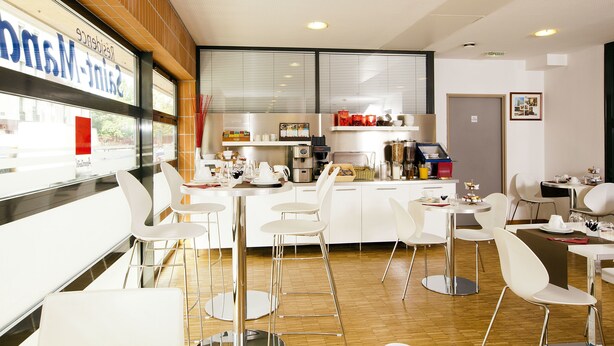 A modern cafe with white furniture, a coffee machine, and a view of the street outside. - Séjours & Affaires Montreuil Saint Mandé (Montreuil)