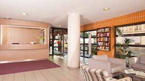 A hotel lobby with a reception desk, seating area, and a bookshelf. - Séjours & Affaires Montreuil Saint Mandé (Montreuil)