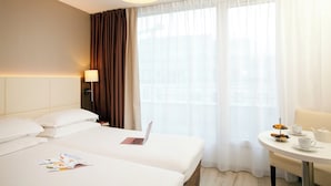 A hotel room with two beds, a laptop on one bed, a table with a teapot and cups, and a window with sheer curtains. - Séjours & Affaires Montreuil Saint Mandé (Montreuil)