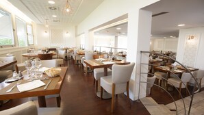 A spacious restaurant with multiple dining areas, wooden tables, white chairs, and a modern interior design.