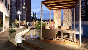 Un'area patio esterna con una pergola in legno, posti a sedere e piante in vaso.