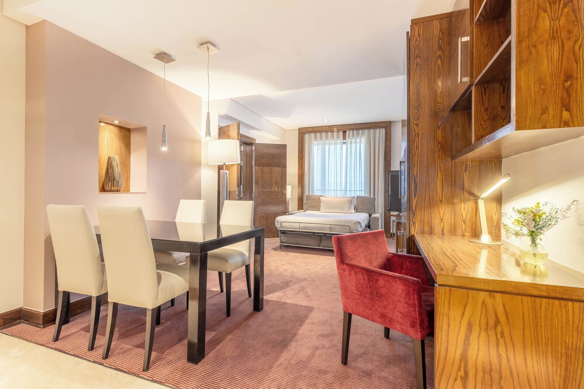 Een hotelkamer met een zithoek, een bed, een rode stoel en een houten kast.