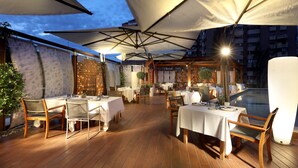 Un'area pranzo all'aperto con tavoli e sedie, riparata da grandi ombrelloni, e un pavimento in legno.