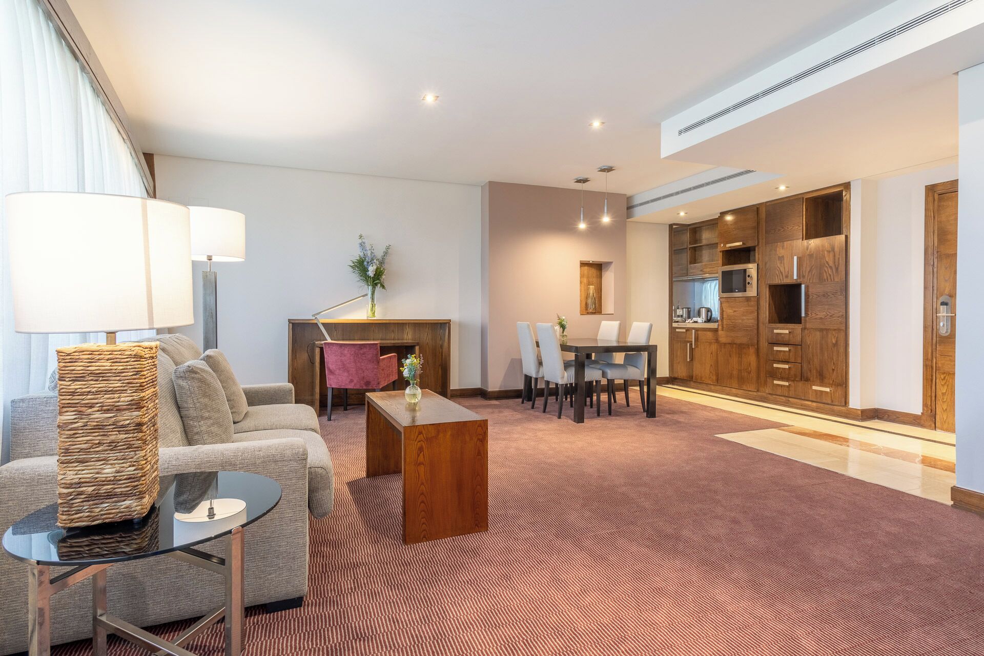 A modern hotel room with a living area, a dining table, and a kitchen area.