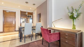 Una cocina moderna con electrodomésticos integrados, un comedor con una silla roja, y un escritorio con una lámpara y un florero.