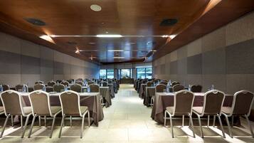 Un salón de conferencias con filas de mesas y sillas, ventanas amplias y techo de madera.
