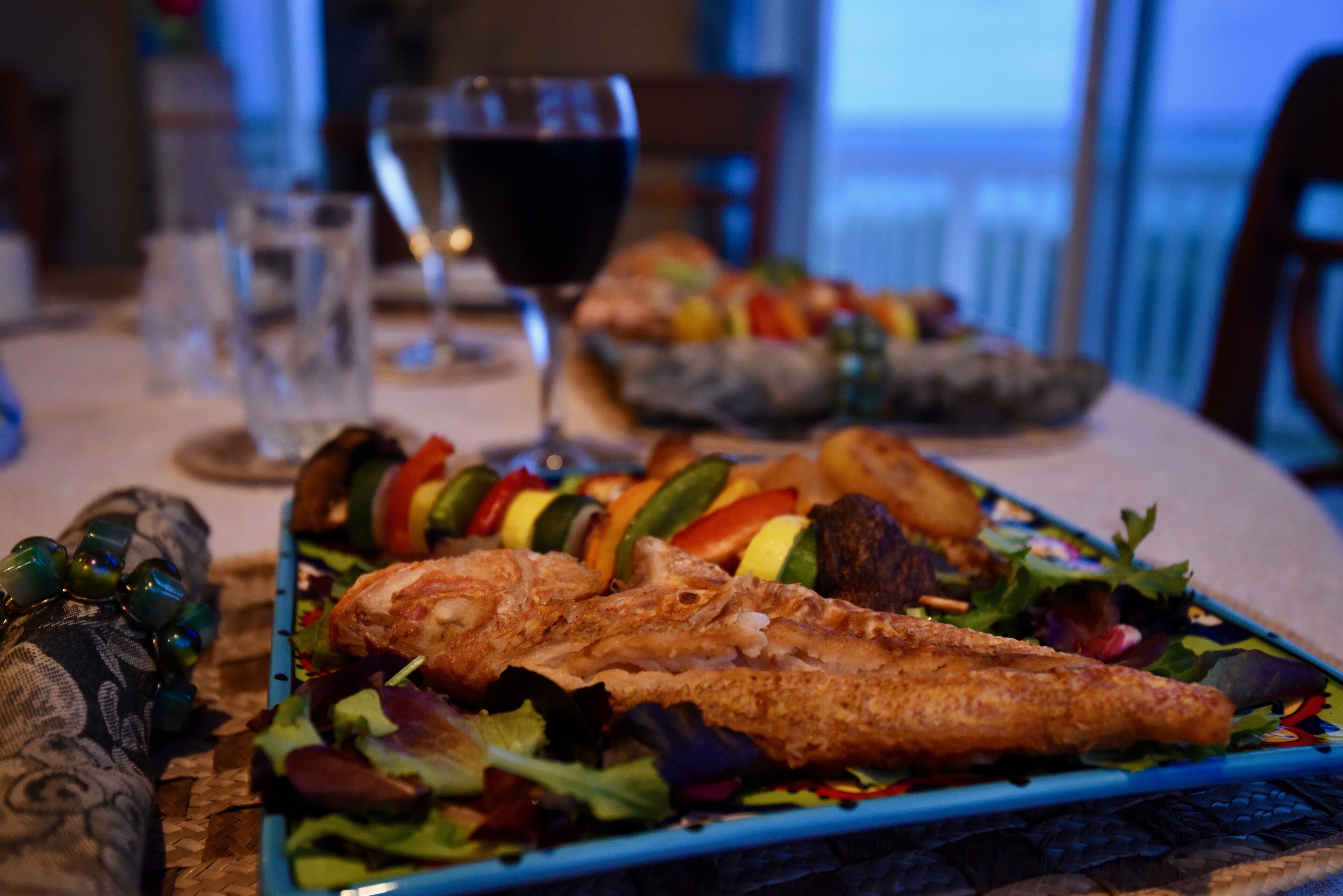 A dining table with a seafood dish, a glass of red wine, and a bowl of salad.