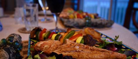 A dining table with a seafood dish, a glass of red wine, and a bowl of salad.