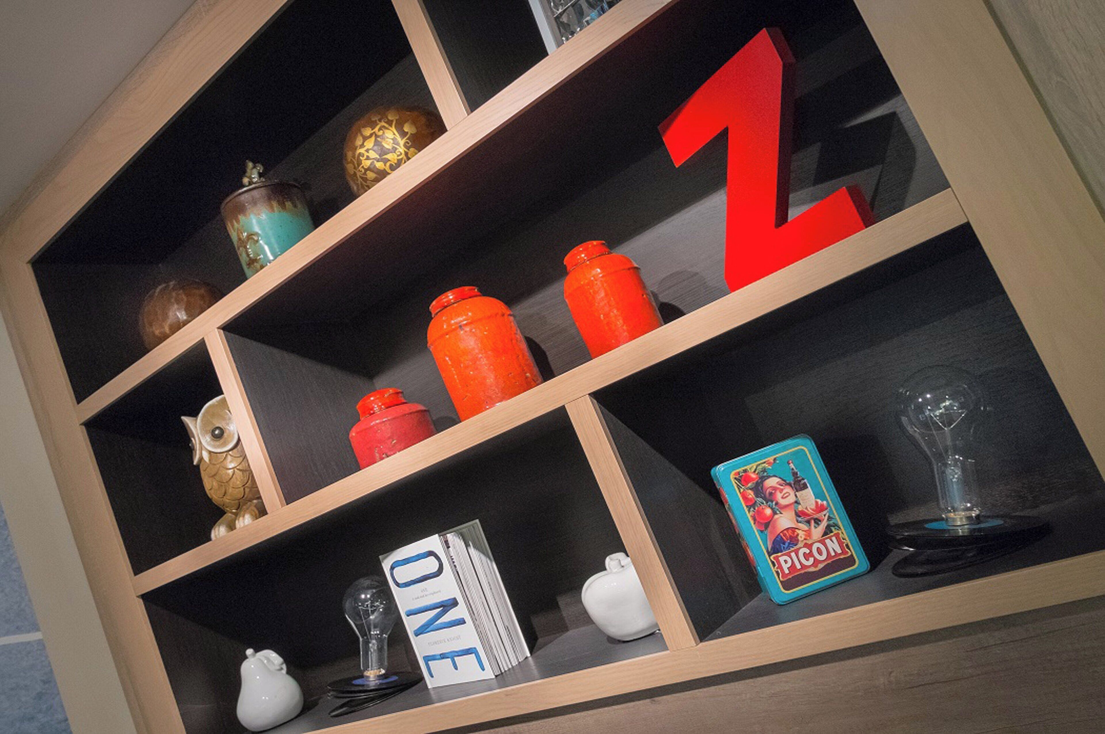 Una estantería de madera con varios objetos decorativos, incluyendo una gran letra 'Z' roja, un búho de cerámica blanca y una tarjeta azul con la palabra 'PICON'.