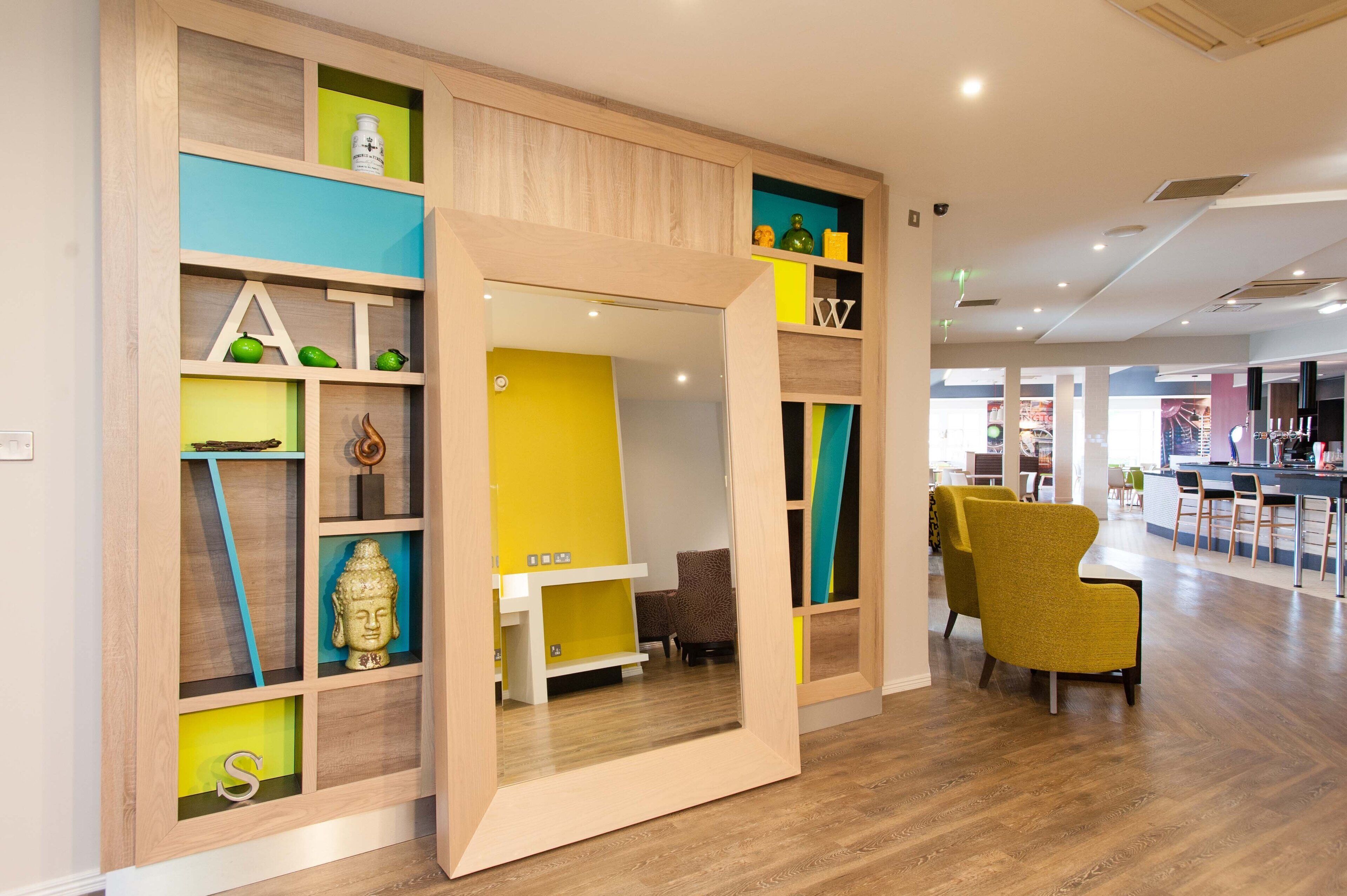 A modern interior with a wooden partition, a yellow accent wall, and a bar area in the background.